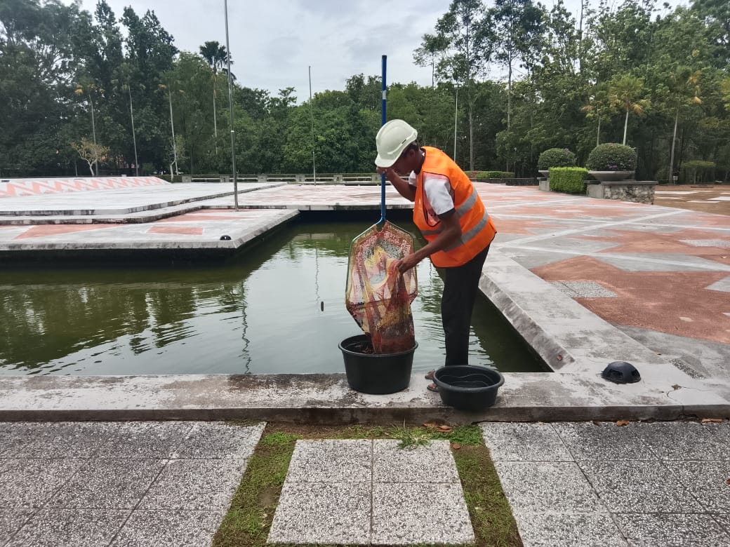 A worker with the new contractor sifts out the moss and other flotsam from the water in the moat.